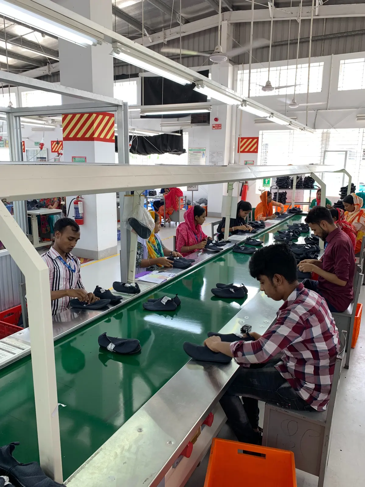 Workers sit along a green conveyor line on a factory floor.
