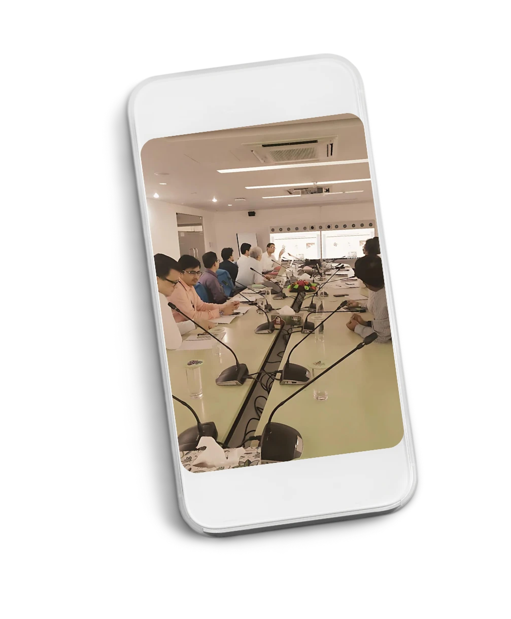 A policy roundtable seen on a mobile phone: participants seated along a long conference table with microphones